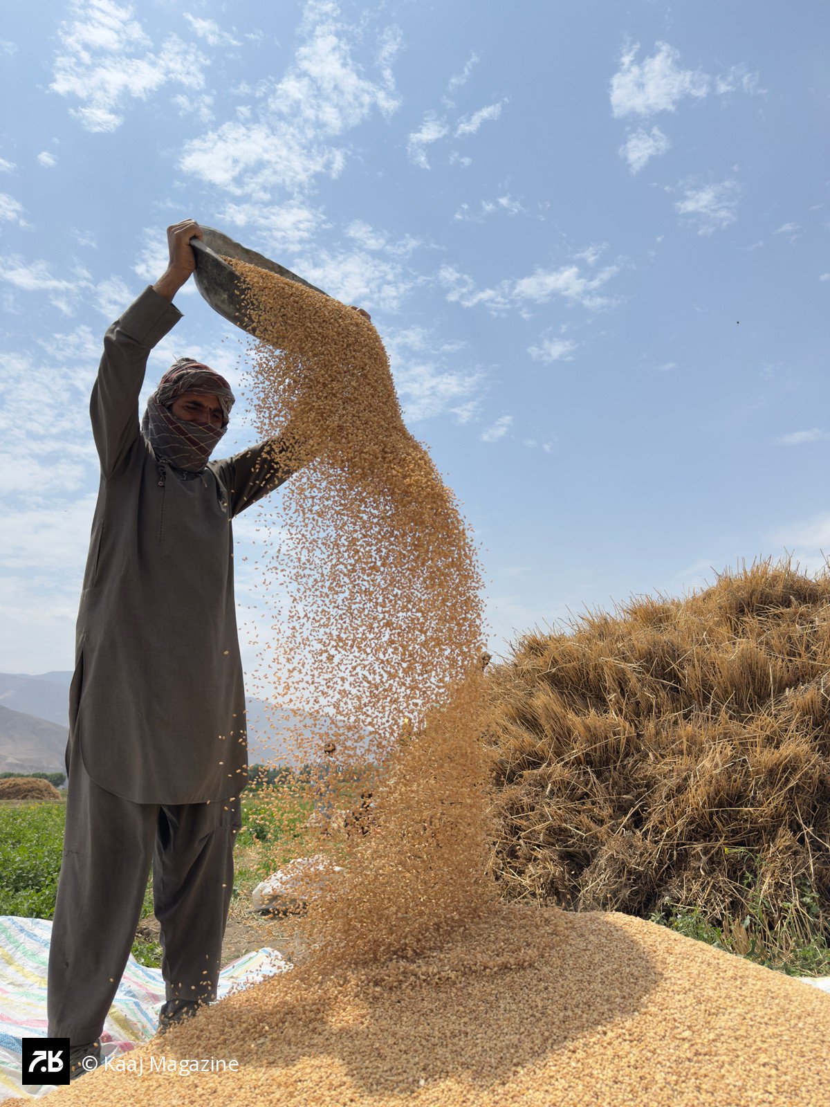 Farmer winnowing grain under a blue sky