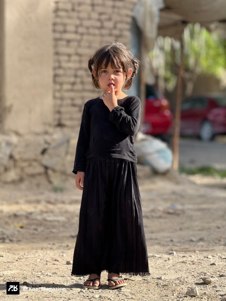 A young girl stands outside a residential building, wearing a long black dress