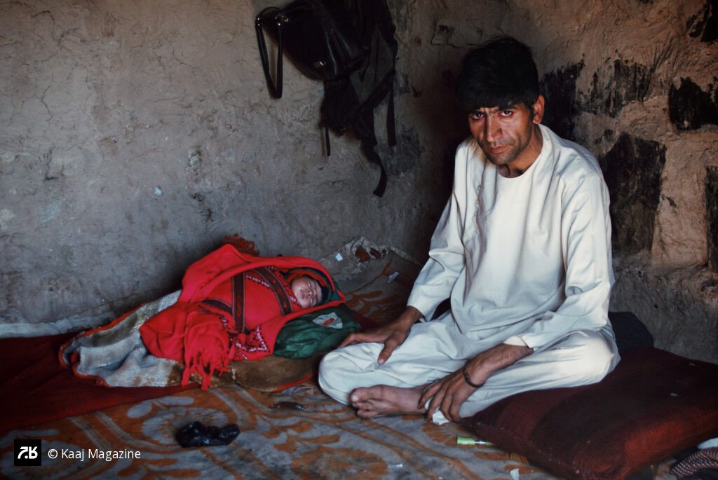 A man sits beside a sleeping infant inside a modest earthen home