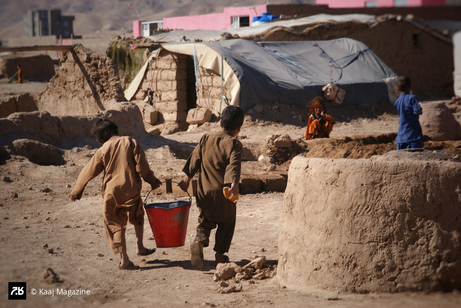 Two little boys carrying a red bucket through camp