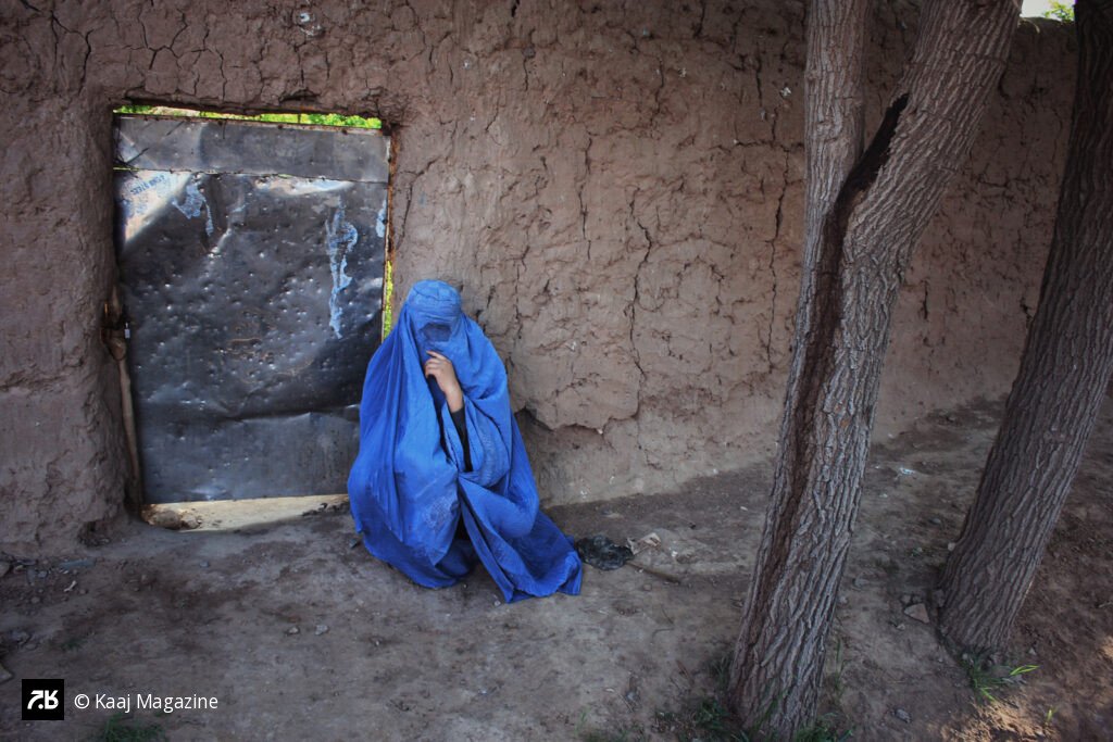 Woman in burqa sitting outside a mud wall